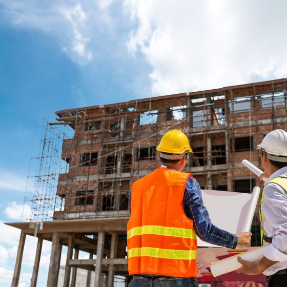 Businessman engineer looking blueprint in a building to  discussion with architects at construction site or building site of highrise building